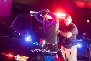 Man with his hands on his head getting arrested by a police officer next to police car